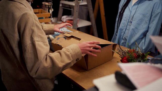 Staff Opening Shipment Box On Counter, Inspecting Garments And Tags For Quality And Display