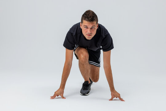 Athletic man in sportswear starting a sprint from a crouched position on a light studio background, demonstrating speed, strength, fitness, training, and dynamic movement.