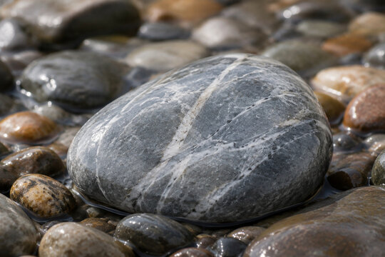 A smooth soapstone rock rests among wet river pebbles.