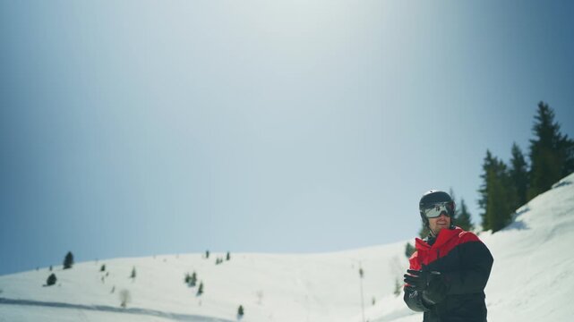 A man in ski gear, including a helmet and goggles, stands on a snowy mountain slope. He enjoys the winter landscape and sunny weather, ready for active outdoor fun.