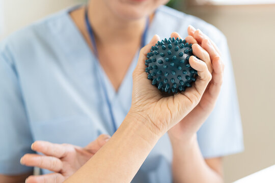 Close up of a physical therapist helping a patient exercise with a spiky massage ball for hand rehabilitation, occupational therapy and stroke recovery medical concept.