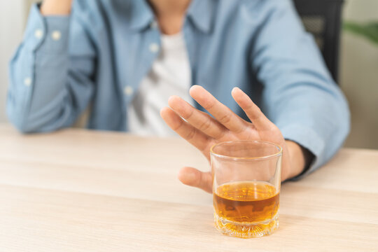 Close up of Asian young man making stop hand gesture to refuse a glass of whiskey, responsible man saying no to alcohol drink, stop alcoholism and addiction social problem, health care concept