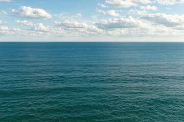 Fototapeta premium Vast blue ocean horizon under a bright sky with scattered white clouds on a sunny summer day