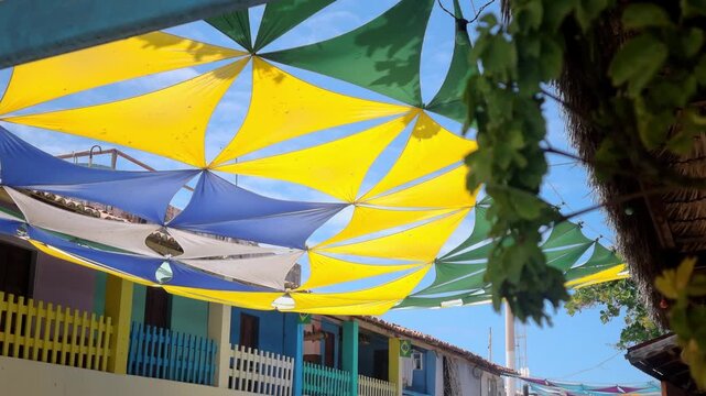 Colorful fabric sun shade sails in Brazilian national colors stretched over street in Canoa Quebrada