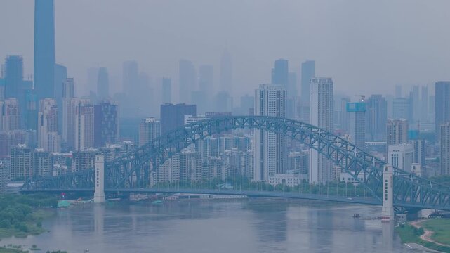 Wide aerial view of a steel arch bridge over a river with a modern city skyline in the background in Chongqing, China