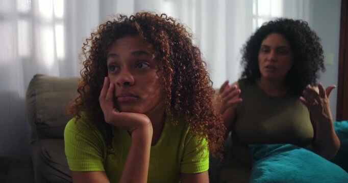 Frustrated mother gesturing while teenage daughter looks away in boredom, showcasing family conflict, communication struggles, and emotional tension, African descent