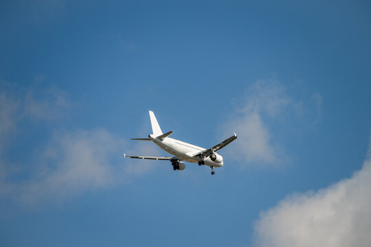 A white passenger airplane descends through a blue sky with soft white clouds, preparing for landing with its gear extended.