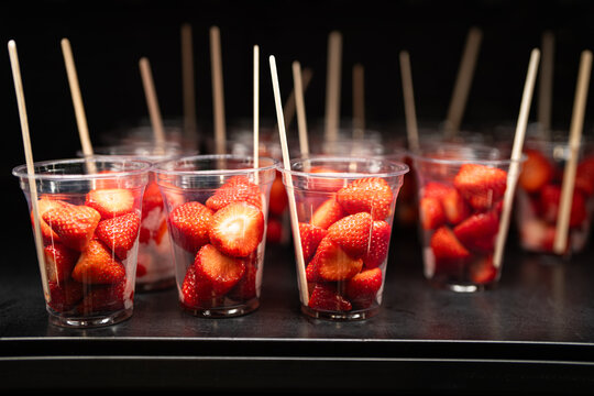 Fridge in restaurant filled with plastic cups portions full of fresh aromatic strawberries for sale, sliced strawberries served in cups standing on shelf in refrigerator, cafe selling healthy desserts
