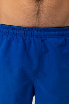 Close-up shot of a man's lower stomach and the elastic waistband of bright blue athletic shorts. Focus on fabric texture, stitching detail, skin, and hair. Ideal for sports and apparel design.