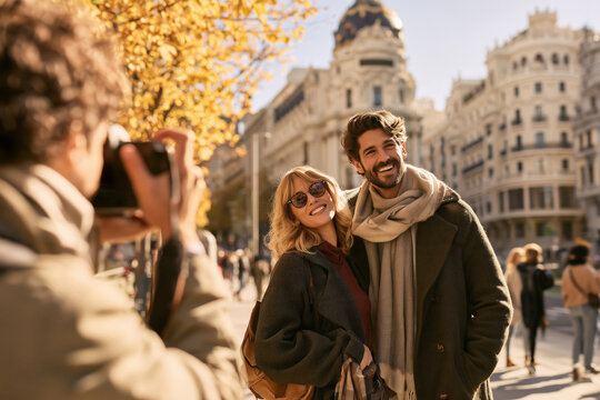Professional photographer taking pictures of a smiling couple in Madrid during a warm autumn photo session on a sunlit city street