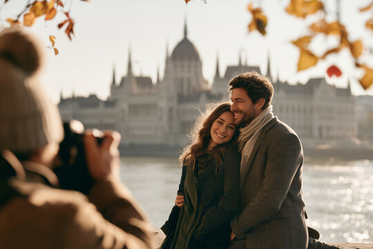 Professional photographer taking pictures of a smiling couple in Budapest during an autumn travel photo session with the Hungarian Parliament in the background