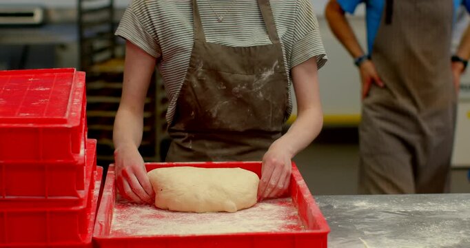 close-up of baker torso and hands pressing and shaping round dough ball on heavily floured red tray, flour dust coating tray in commercial kitchen at eye level