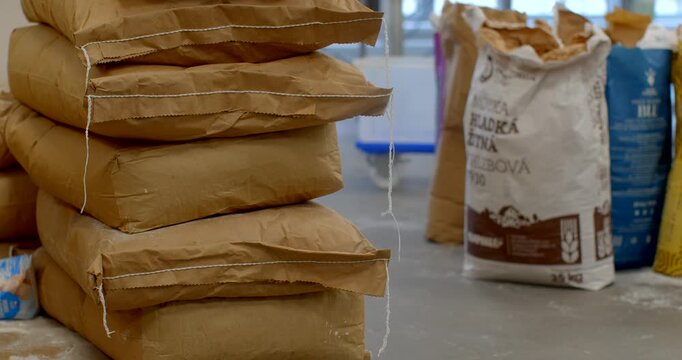 crumpled brown kraft paper sacks with sewn seams rest on cardboard-covered wooden pallet, tied with loose white twine in indoor storeroom, readily for shipment