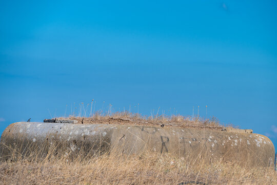 A weathered concrete military pillbox bunker sits embedded in dry grass on a ridge under an expansive, clear blue sky.