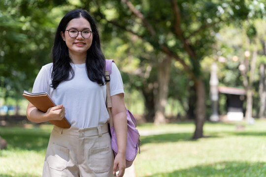 Young university student carrying books and a backpack outdoors on a sunlit park path, illustrating education, reading, mobility and an active lifestyle with useful copy space.