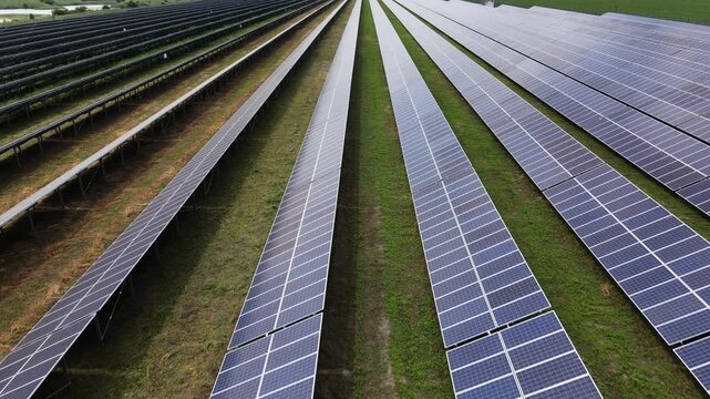 Aerial view of a solar farm with long rows of photovoltaic panels producing clean renewable energy on a green field