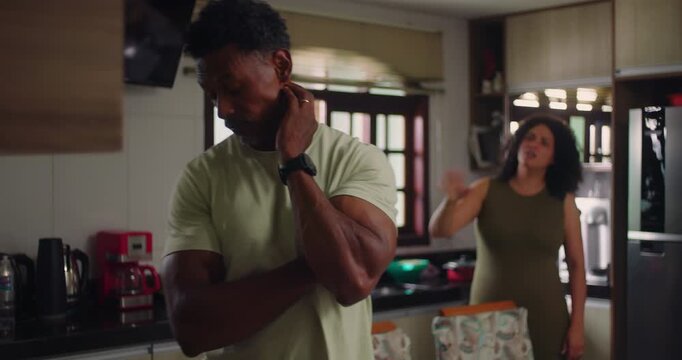 Man standing in foreground with defensive posture during argument, wife expressing anger in background, showcasing strained communication and relationship conflict