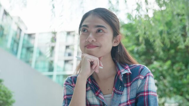 Young woman sits outdoors in a leafy setting, resting her face in her hands and changing expressions, creating a versatile lifestyle scene for reflection, emotion, wellness, and personal moments