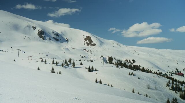 A single skier carves down a wide, snow-covered mountain slope on a bright winter day. Enjoy the scenic view of this beautiful alpine landscape and clear sky.