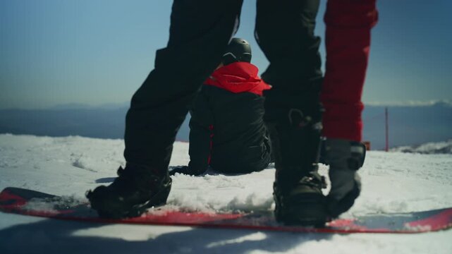 Friends prepare their snowboards on a sunny winter day, high on a mountain. They enjoy the fresh snow and clear blue sky together.