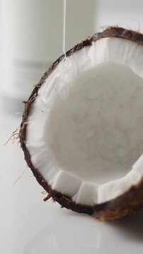 Pouring fresh coconut water into a split coconut shell isolated on a white background with tropical ingredients for skincare