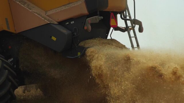 Combine harvester ejecting chopped straw during harvesting in a field, slow motion close-up of agricultural machinery