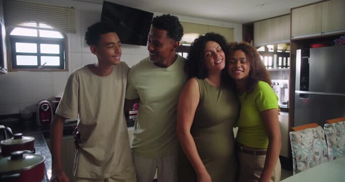 Happy family of African descent posing together in modern kitchen, father and mother with teenage son and daughter, standing around table, family bonding moment