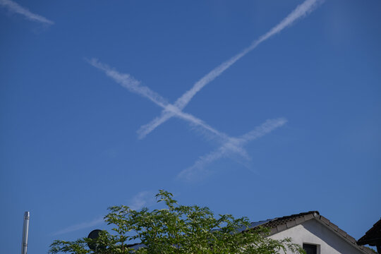 Zwei Kondensstreifen kreuzen sich am blauen Himmel &uuml;ber einem Wohnhaus.