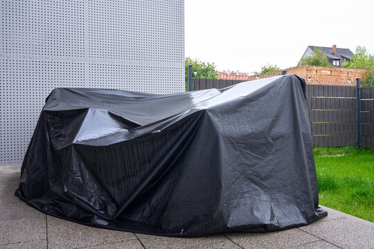 Outdoor furniture covered with wet black tarp on patio after rain