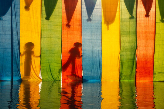 Silhouette of two Intha Fishermen in boats standing Behind Colourful lotus silk Fabrics drying at Inle Lake, Shan State, Myanmar