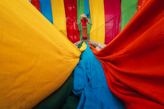 Rear view of a woman standing on the stern of a boat hanging Handcrafted colourful lotus silk, Inle Lake, Shan State, Myanmar