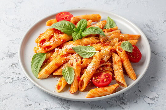 Classic italian pasta penne alla arrabiata with basil and freshly grated parmesan cheese on dark table. Penne pasta with chili sauce arrabbiata.