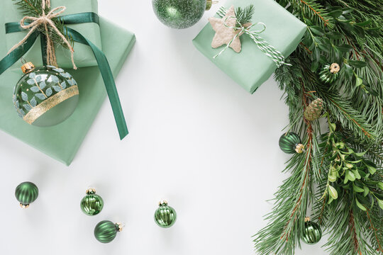 Overhead view of three wrapped Christmas gifts, festive Christmas baubles and assorted foliage on a white table