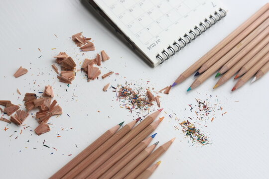 Overhead view of a diary, assorted colour pencils and pencil shavings on a white background