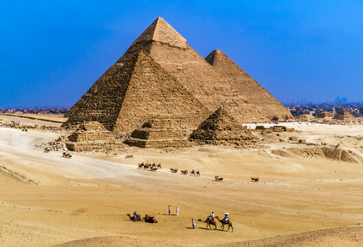 Aerial view of Camel trains walking towards the Giza Necropolis (The Pyramid of Khafre, Pyramid of Khufu and Queens' Pyramids), Giza, Cairo, Egypt