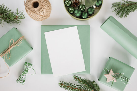 Overhead view of a blank card on a wrapped Christmas gift surrounded by twine, a ball of string, fir branches, Christmas gift boxes and Christmas baubles on a white table