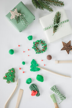 Overhead view of wrapped Christmas gifts decorated with fir branches on a white table with assorted wooden tools and air dry clay Christmas tree and wreath decorations
