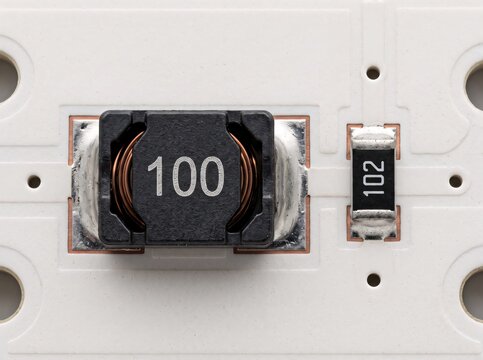 SMD inductor labeled 100 on white circuit board next to resistor 102.