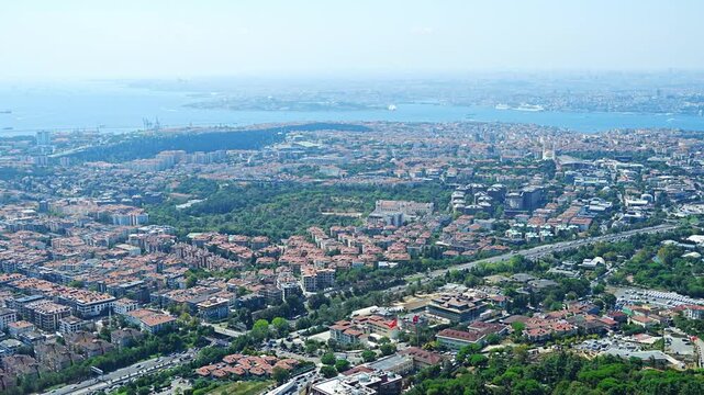 Aerial view of Istanbul cityscape featuring residential buildings, green parks, and the Bosphorus Strait with ships in the distance in Istanbul, Turkey 