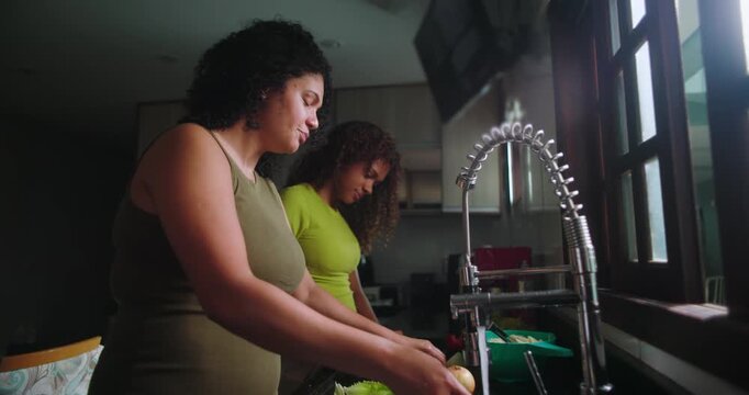Family gathered in the kitchen with the mother washing vegetables, the teenage daughter helping, and the father observing, preparing for a shared family meal