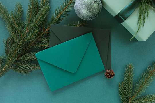 Overhead view of two blank envelopes, evergreen fir branches, a Christmas bauble and pinecone on a green background with a wrapped Christmas gift