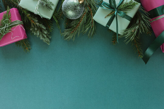 Overhead view of assorted wrapped Christmas gift boxes decorated with evergreen sprigs, jute twine and velvet ribbon arranged at the edge of a green background
