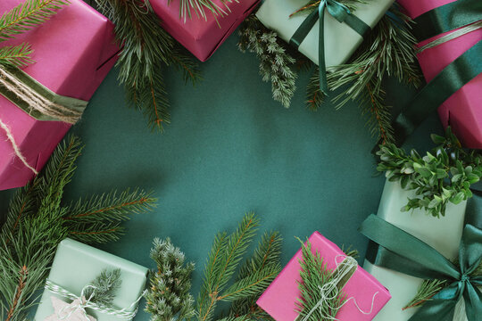 Overhead view of assorted wrapped Christmas gift boxes decorated with evergreen sprigs, jute twine and velvet ribbon arranged in a border on a green background