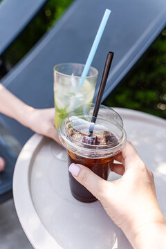 Close-up of two people sitting on sun loungers drinking a mojito cocktail and iced coffee on a summer day