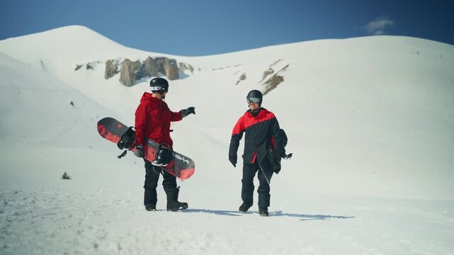 Two male snowboarders walk uphill on a snow-covered mountain, carrying their boards. They are preparing for an adventurous ride down the pristine winter landscape.