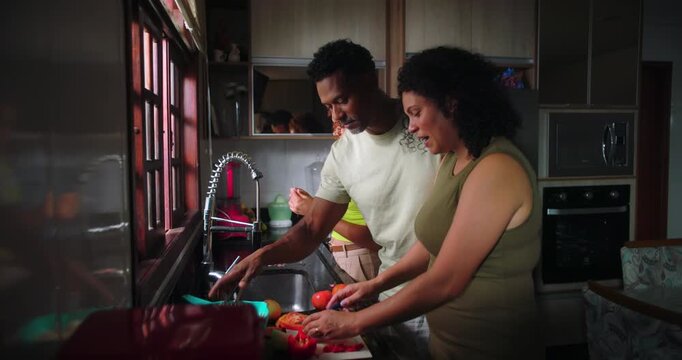 Family working together in kitchen, mother slicing vegetables, father standing nearby, teenage daughter assisting, sharing a bonding moment during meal preparation