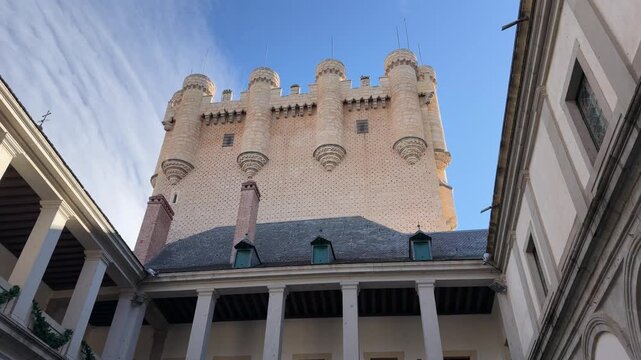 Low angle shot capturing the monumental Alcazar castle tower with ornate medieval architecture and stone courtyards under a bright sunny winter sky in Segovia, Spain.