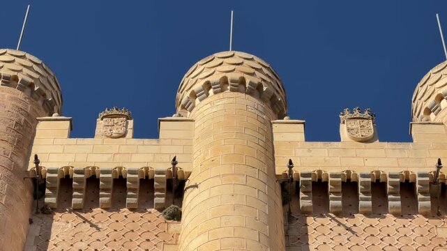 Tilt up shot showcasing the intricate stone facade, ornate medieval crenellations, and historic fortress architecture of the Alcazar castle in Segovia, Spain.