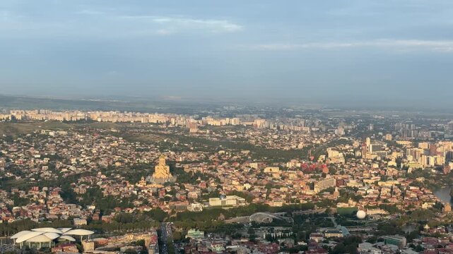 Tbilisi, Georgia - September 01, 2026: Aerial perspective of Tbilisi showcasing city buildings, a river, and surrounding hills under a sunset sky