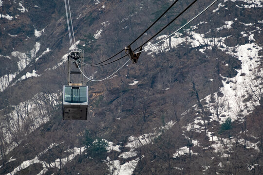 Overhead cable car above a rugged mountain slope with bare trees and melting patches of snow in winter, Seoraksan National Park, South Korea